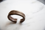 Side profile of an antique bronze cuff showing its raised stripes and hand-worked texture.