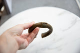 A hand holds the antique African bronze cuff, showing its curved profile and texture.