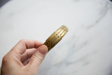 The aged, golden patina and striped surface of the antique bronze cuff.