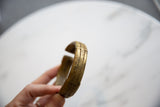 Hand holding an antique bronze cuff bracelet, highlighting its curved shape and patina.