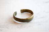 The curved, open design of an antique African bronze cuff with a textured stripe pattern.