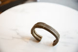 A dark bronze African cuff bracelet showing its sculptural open form and striped texture.