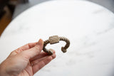 Hand holding an antique African aluminum cuff with a twisted band and geometric detail.