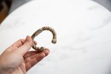 Hand holding an antique African cuff showing its twisted aluminum body and shape.