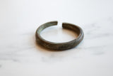 The distinct diagonal seam and oxidized patina on an antique African bronze cuff.