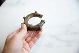 A hand holding an antique African bronze cuff, highlighting its profile and textured details.