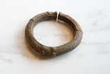 Three-quarter view of an antique African bronze cuff with textured geometric patterns.