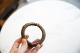 Hand holding an antique African bronze cuff, showing its open circular shape.