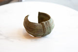 Curved shape and central braided detail of an antique oxidized bronze cuff bracelet.