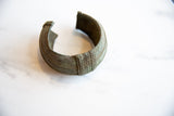 Angled view of an antique bronze cuff showing its open shape and textured geometric band.