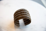 Close-up of African bronze cuff with triangular and scallop patterns, rich patina.