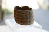 Ribbed bands and raised geometric motifs on the patinated surface of an antique bronze cuff.