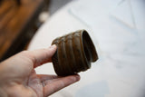 Antique African bronze cuff held in hand, showing its wide, ribbed form and opening.
