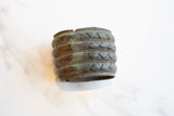 Aged green patina over raised geometric detailing on an antique bronze cuff.