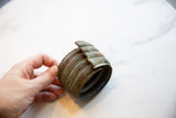 Hand holding the antique bronze cuff to show its scale and time-worn, patinated surface.