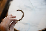 The curved C-cuff shape of an antique African bronze bracelet with a time-worn patina.
