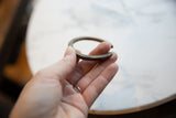 A hand holds the antique African bronze bracelet, displaying its size and patina.