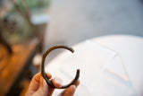 Handmade antique bronze cuff held, showing its simple, open shape and dark patina.