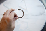 A view of the antique copper cuff's simple C-shape and aged patina held in hand.