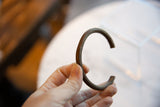 Hand holding the antique C-shaped copper bracelet, showing its aged patina and scale.