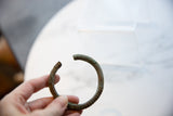 The C-shaped profile and aged, textured surface of an antique African bronze bracelet.