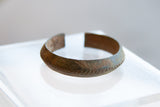 Angled profile of an antique bronze alloy bracelet highlighting its aged, textured patina.