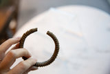 A hand holding the antique copper cuff to show its rich patina and striped texture.