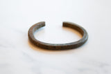 The rustic, open C-shape of the handmade antique African bronze bracelet.