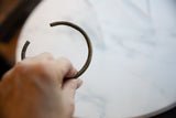 A hand holds the antique bronze cuff to display its striped texture and open shape.
