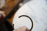 The open, curved form and striped texture of an antique bronze cuff.