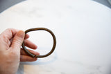 Hand holding an antique African bronze bracelet showing its circular form and faded detailing.