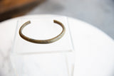 Angled view of a handmade bronze cuff showing its aged, mottled surface patina.