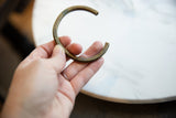 A hand holds the antique bronze African cuff, detailing its aged patina and open C-shape.