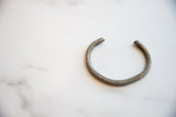 The curved form and rustic, aged surface of a collectible African aluminum cuff.