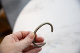 The aged texture and C-shape of the antique aluminum cuff bracelet held in hand.