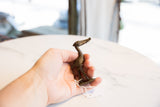 A hand holding the small vintage bronze stork, showing its handmade texture.