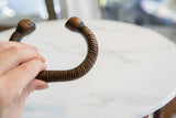 The C-shape and scale of an antique copper snake cuff bracelet held in hand.