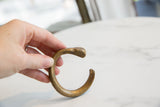 The open C-shape and aged patina of an antique African bronze snake bracelet.