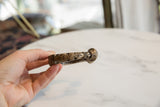 The rounded terminal of an antique aluminum cuff showing its aged, mottled patina.