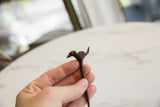 Vintage African bronze bird pin held in hand to show its handmade texture and scale.