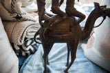Vintage African bronze camel's back, showing warriors' legs and saddle details.
