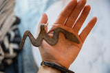 Vintage African bronze snake medallion held in hand, showing its scale and rustic texture.