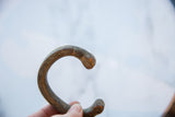 Curved snake head terminal of an antique copper alloy bracelet with a dark, aged patina.