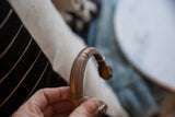 A hand holding the curved section of the antique copper alloy cuff bracelet.