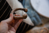 A hand holds the antique copper snake cuff, highlighting its solid form and warm patina.
