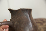 Vintage African wooden pitcher: detail of textured dark wood, visible crack, and chipped rim.