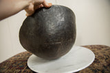 A hand holds the vintage black wooden bowl, revealing its aged, textured surface.