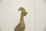 Aged bronze bird's head, showing the textured comb, eye, and open beak.