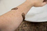 Antique copper snake bracelet with a smooth patina shown worn on a forearm.
