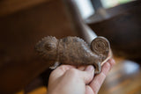 Textured handmade African bronze chameleon with one leg, held in a hand.
